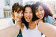 © Xavier Lorenzo - Three multiracial young women having fun on city street. Millennial group of female friends enjoying summer vacation taking selfie portrait outdoors. Friendship and youth concept.