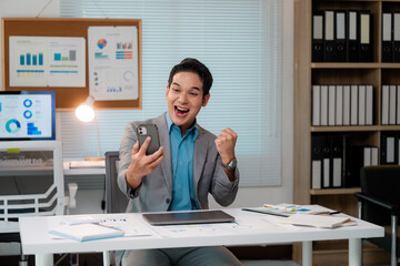 Poster - Excited asian businessman celebrating success while looking at smartphone in office