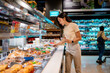 © Parichat - Young woman choosing food from display in supermarket deli section