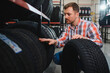 © Serhii - Portrait young man customer examining brand and product characteristics while buying new tires in auto department of dealership. Male client choosing car accessories shopping mall