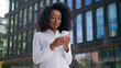 © Yuliia - African American woman chatting message online digital device using mobile phone smartphone social media looking at camera smile female girl businesswoman texting business city outdoor employer worker