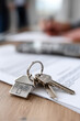 © Emanuel - House-Shaped Keychain Attached to Keys on a Table, with a Couple Signing Documents at a Desk Behind Them