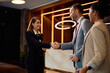 © Drazen - Happy female concierge greeting business couple in hotel lobby.