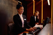 © Drazen - Happy black hotel manager using desktop PC while working at reception desk.