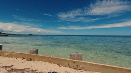 Wall Mural - Timelapse of scenic view of crystal blue water  and sandy beach with wooden barriers