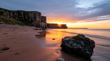 Aufkleber - A serene coastal view at sunset featuring a sandy beach, imposing cliffs, and the ocean with a warm glow from the setting sun. The reflections on the wet sand and the dramatic sky enhance the