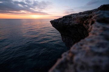 Aufkleber - Dramatic ocean view with focus on rocky coastal edge bathed in the warm glow of the setting sun, creating a scenic seascape with tranquil waters reflecting the colorful sky. The rock formation
