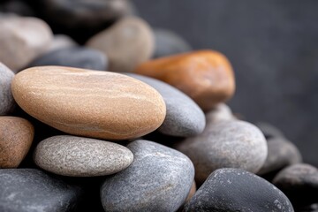 Poster - A close-up shot of an assortment of smooth, rounded rocks in varied shades of gray, beige, and brown against a dark gray background, creating a natural and textured composition