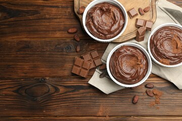 Wall Mural - tasty pudding in bowls, pieces of chocolate and cocoa beans on wooden table, flat lay. space for tex