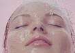 © Danila - A woman stands against a pink backdrop, wrapped in a towel, and tosses water onto her face with her eyes closed