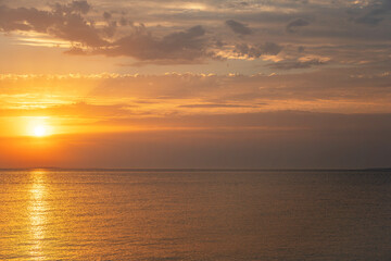 Wall Mural - A breathtaking sunset casts golden hues across a calm sea, painting the sky with warm tones and tranquil beauty.