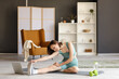 © Pixel-Shot - Beautiful young woman with laptop doing yoga on mat in living room