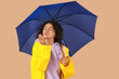 © Pixel-Shot - Happy young African-American woman in raincoat with umbrella blowing kiss on beige background