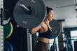 © 2B - Woman performing barbell squat in modern gym during daytime workout session