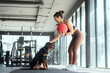 © 2B - Woman exercises with a weighted ball while a dog watches in a modern gym setting during a daytime workout