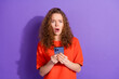 © deagreez - Surprised young woman with curly hair reacting emotionally to phone message against a vibrant purple background.