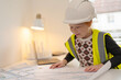 © Iryna - Young child engaged in a creative building activity in bright room while wearing safety helmet and vest during a learning session about architecture