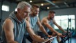 © natakot - An older man with gray hair intently reviews his workout stats on a tablet, flanked by two younger men cycling vigorously. This dynamic scene captures the essence of fitness and determination