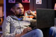 © DC Studio - African american adult working remotely from his apartment on laptop, focusing on tasks completion while he lays on a bean bag. Blending productivity and relaxation, browsing the web.