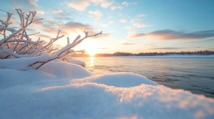 Leinwandbilder - A serene landscape features a snow-covered foreground, a frozen body of water reflecting the warm glow of the setting sun, and distant trees silhouetted against the light blue sky with scattered