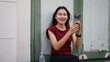 © pixs4u - Young Asian woman sitting outside in urban environment, grinning while holding handheld fan and enjoying breeze during hot summer day, showing natural and relaxed expression