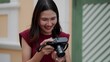© pixs4u - Closeup of young Asian woman smiling with joy while reviewing photos on digital camera outdoors, expressing genuine happiness and creativity in a casual and stylish lifestyle setting.