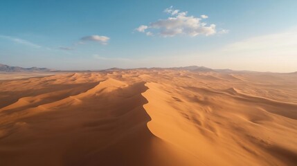 Poster - Aerial view of desert landscape under a clear blue sky with minimal cloud cover. Sand dunes and structures are visible in the distance. The lighting suggests a sunset or sunrise