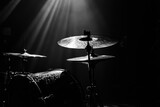 A dramatic black and white close-up of a drum kit under stage lighting, showing detail and texture.