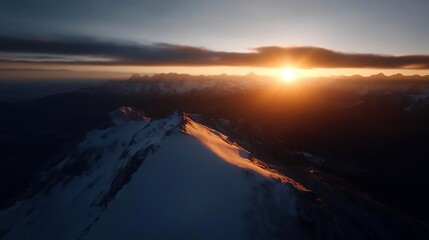 Aufkleber - Aerial view of a mountain range at sunset. The sun illuminates the peaks in shades of orange and gold creating a dramatic landscape. The sky features a mix of dark and light clouds above