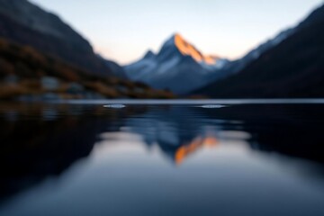 Aufkleber - Serene mountain landscape featuring a reflective lake mirroring snow-capped peaks under a dusky sky. Orange hues illuminate the mountain tops with soft focus