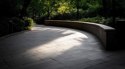 Poster - A curved stone bench casts a shadow on the patterned walkway under dappled sunlight filtering through lush green foliage creating a peaceful atmosphere