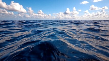 Aufkleber - Low angle shot of vast blue ocean water under a bright sky with scattered white clouds. The light reflects on the water surface creating a serene seascape