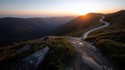 Aufkleber - Scenic mountain landscape at sunset with a winding road illuminated by golden light. A deep valley contrasts with the rugged terrain and clear sky