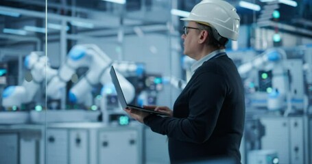 Fototapete - Electronics Factory Manager Working on Laptop at an Industrial Manufacture with Robotic Arms. Specialist in a Hard Hat Monitoring Data on a Computer, Checking and Planning Production Process