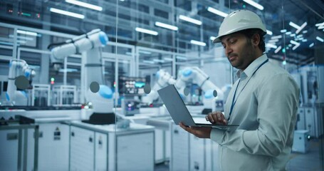 Leinwandbilder - Indian Engineer Working in a High Tech Factory with Robotic Arms Assembling Electronic Components on a Production Line Conveyor Belt. South Asian Man Using Laptop in a Modern Manufacturing Facility