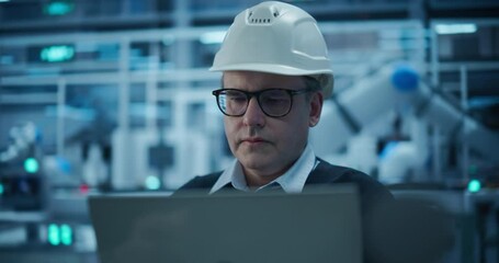 Fototapete - Adult Caucasian Engineer in a Hard Hat Working in a Modern Industrial Facility, Using Laptop Computer to Monitor Robotic Arms in a Futuristic Electronics Manufacturing Factory