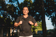 © Mdv Edwards - Southeast Asian man in his 50s stands confidently in a park, geared up with a backpack and ready for rucking exercise.