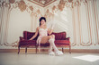 © deagreez - Elegant woman in glamorous corset holding lace fan while seated in luxurious palace interior reflecting classic historical style