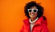 © BeeSee - A young Black woman with curly dark hair wearing large white sunglasses and a bright red puffy jacket, smiling and posing against an orange background  created with generative ai