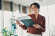 © deagreez - Confident young businesswoman reviewing documents in a bright modern office setting with a clipboard in hand
