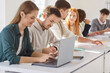 © Studio Romantic - Group of young confident college or university students sitting at the same desk in the classroom during a lesson doing educational project on laptop. Education and knowledge concept.