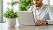© ngstock - Businessman Working on Laptop in Modern Office with Green Plant in Stylish Pot for Productivity and Focused Environment
