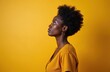 © Vadym - Side profile of black woman with natural afro hair. Wearing gold hoop earrings and yellow blouse, she looks up with focused expression. Set against yellow backdrop.