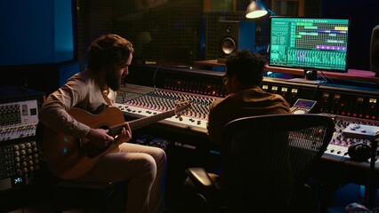 Leinwandbilder - Talented artist doing live performance with his guitar in professional studio, recording new songs with his audio expert. Sound engineer mixing and mastering tracks for him. Camera B.