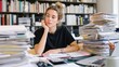 © CStock - A young woman sits at a cluttered desk surrounded by stacks of papers, lost in thought, symbolizing workplace stress and productivity.