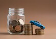 © sujgat - Miniature blue car with stacks of coins, symbolizing auto tax and insurance savings. A glass jar holds money for auto finance and loans. Savings concept designed for car-related financial planning.