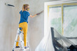 © Denys Kurbatov - Young woman on stepladder cleaning wall after plastering works. Girl in a respirator sweeping a wall during apartment renovation, emphasizing solo repair work
