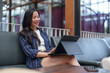 © crizzystudio - Young asian freelancer sitting comfortably on a sofa in a modern coworking space, focused on her work with a digital tablet and keyboard, enjoying remote work flexibility