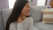 © Krakenimages.com - Woman experiencing neck pain while sitting in her living room on a comfortable sofa, showing a pained expression in a cozy home environment.