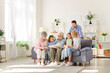 © Studio Romantic - Multi generational extended family reading story together. Grandfather, grandmother, mom, dad and children sitting on sofa in light living room interior in grandparents' apartment and reading book